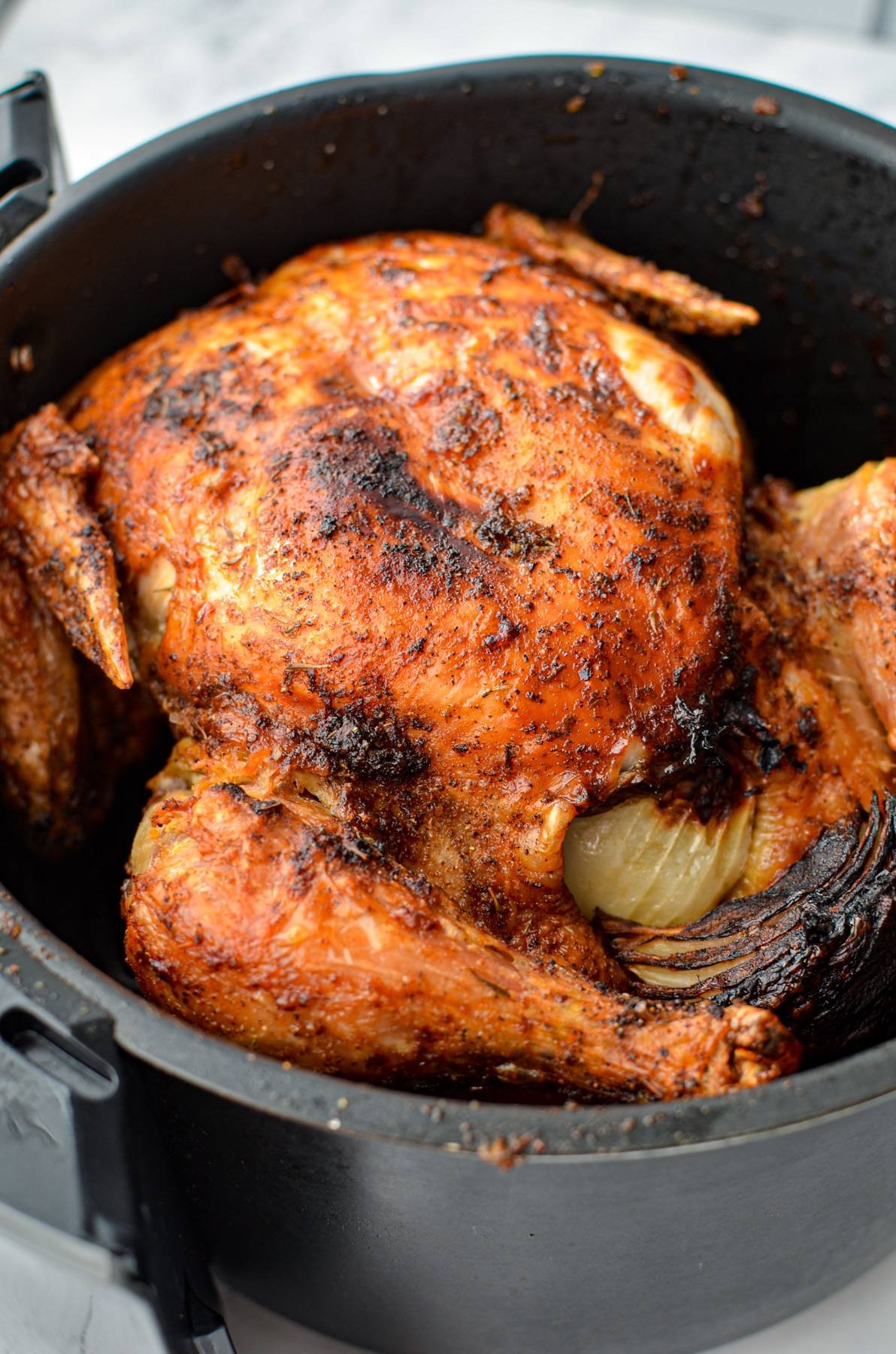 A fully cooked rotisserie chicken inside of an air fryer basket.
