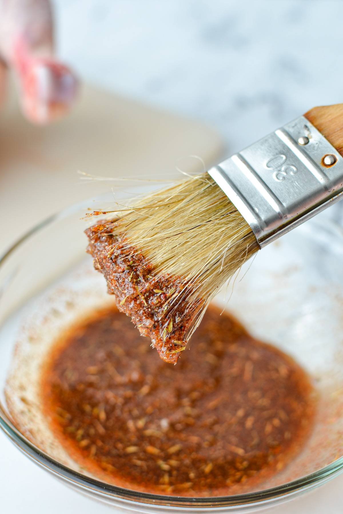 A small bowl of seasoning and oil, with a brush with some of the sauce on it.