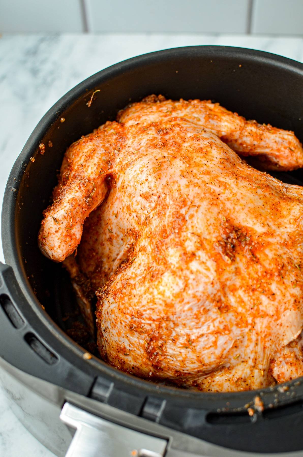 A chicken in an air fryer basket, breast side down.