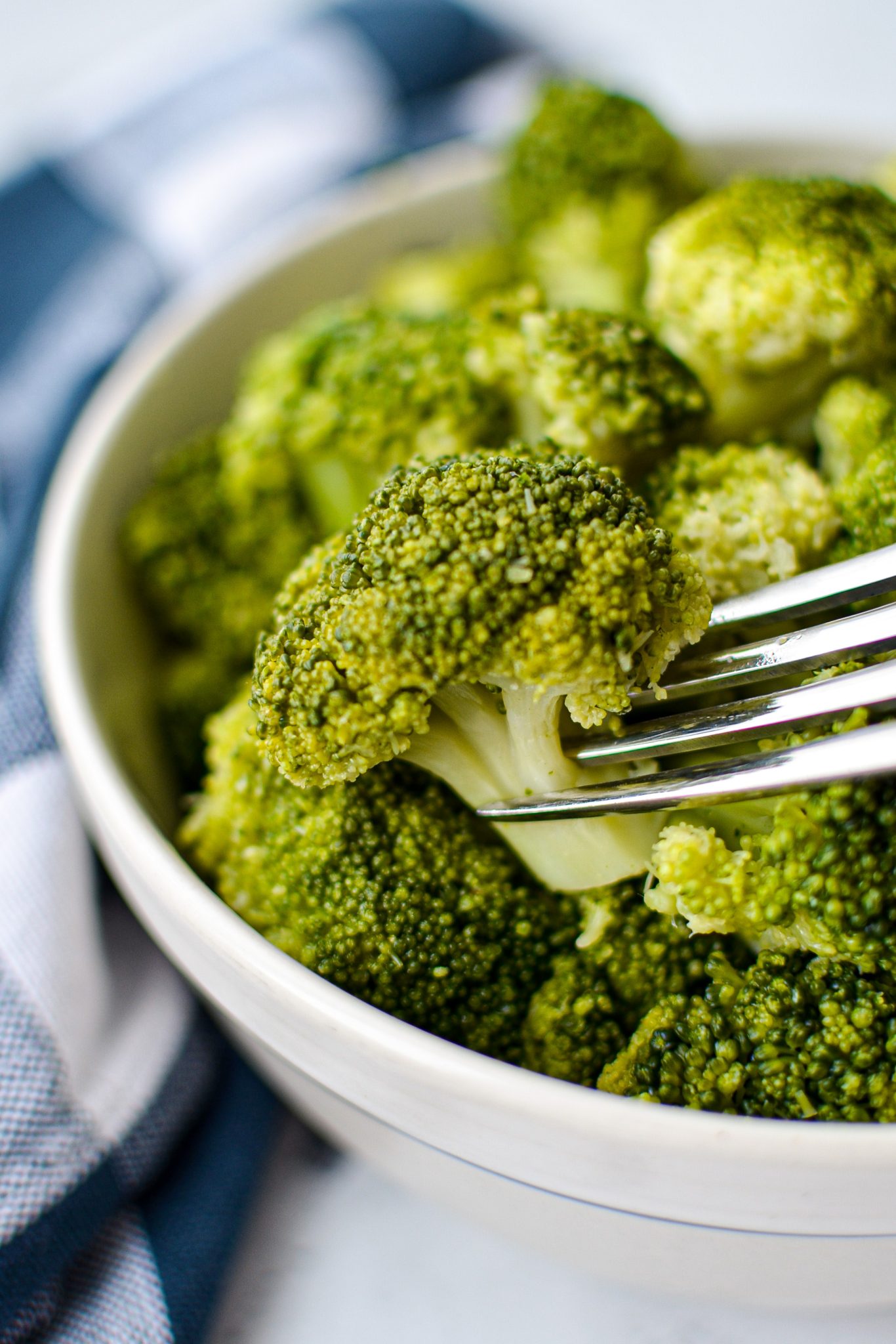 A bowl of cooked broccoli, with a fork taking a piece.
