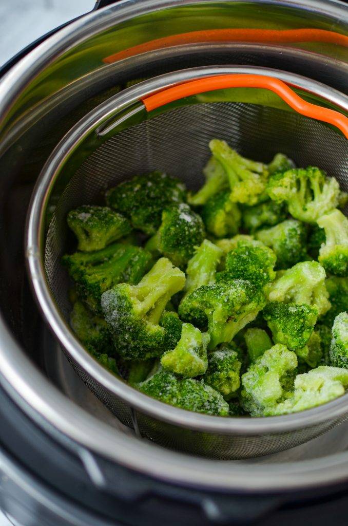 Frozen broccoli resting inside the insert of a steamer basket inside of an Instant Pot.