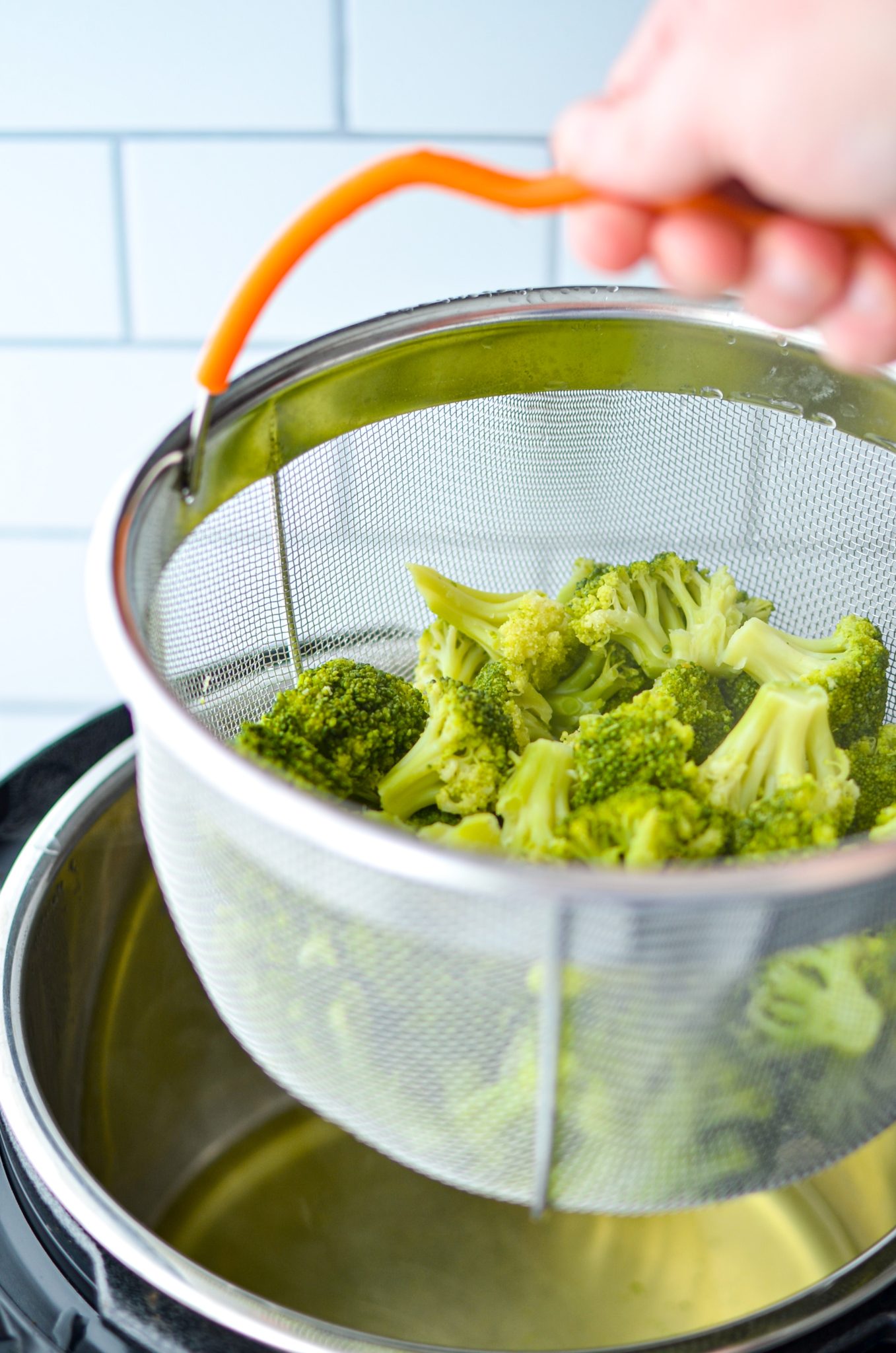 Lifting the steamer basket out of the Instant Pot with cooked broccoli inside.