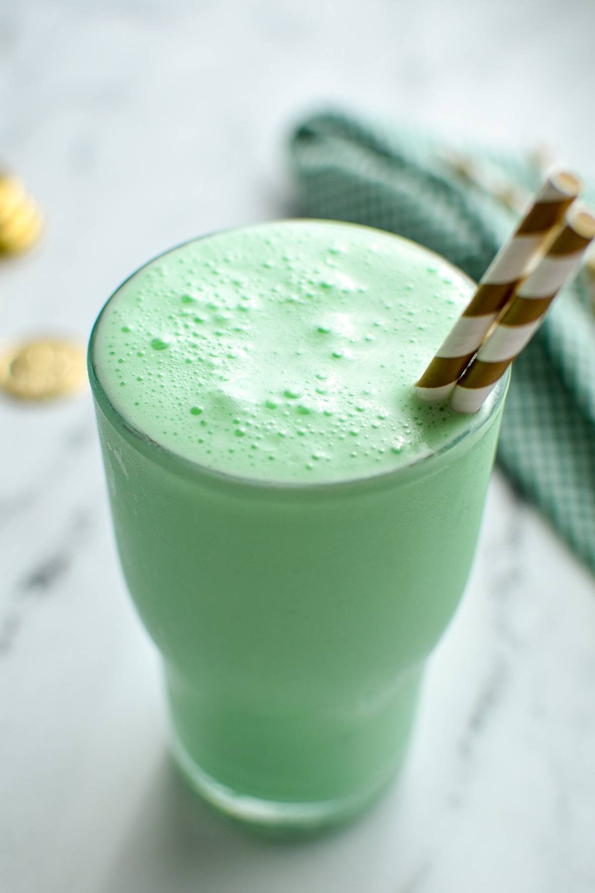 A glass filled with a green milkshake, with a gold striped set of straws sticking out.