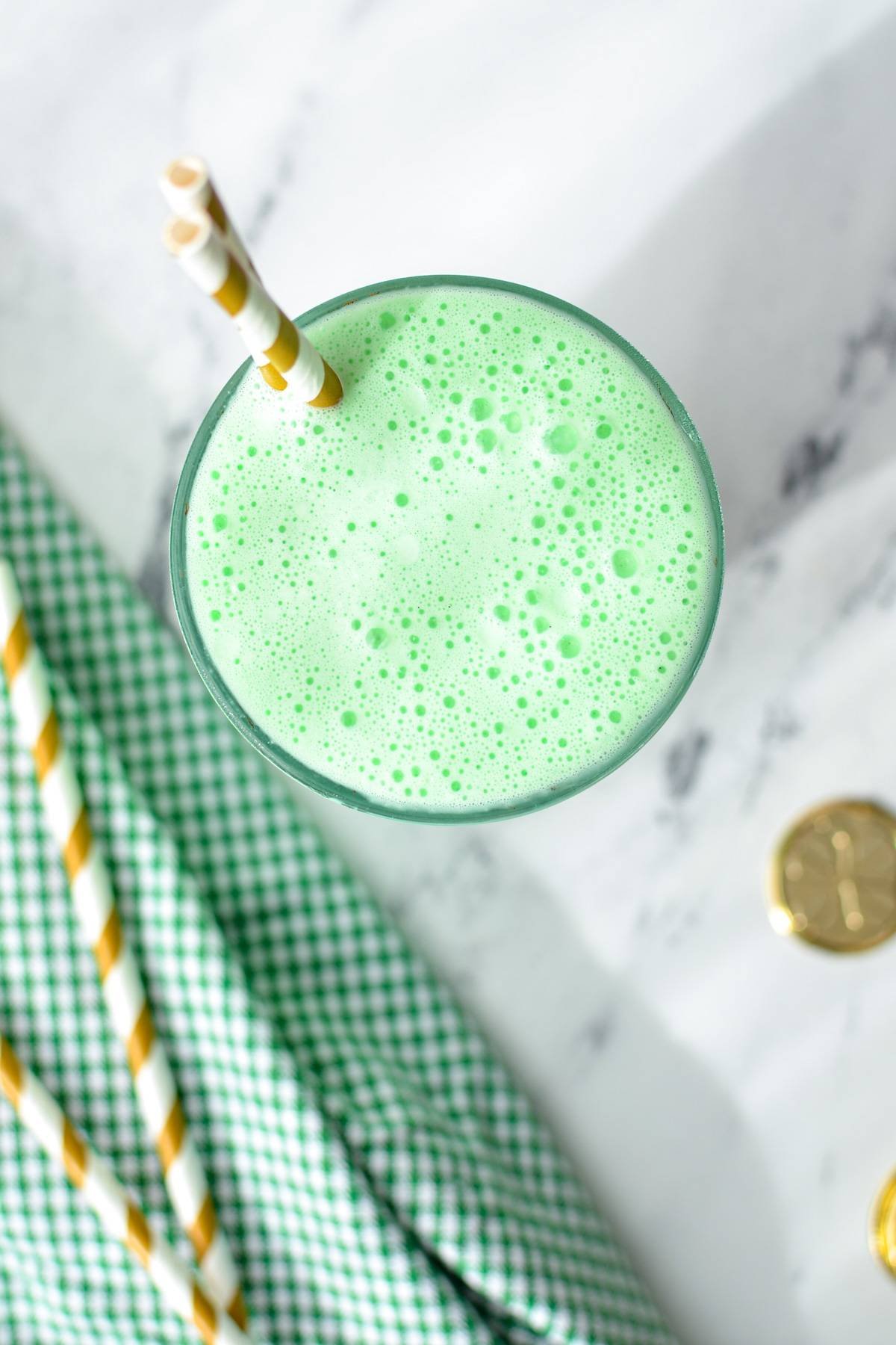 An overhead shot of a green milkshake with gold striped straws.
