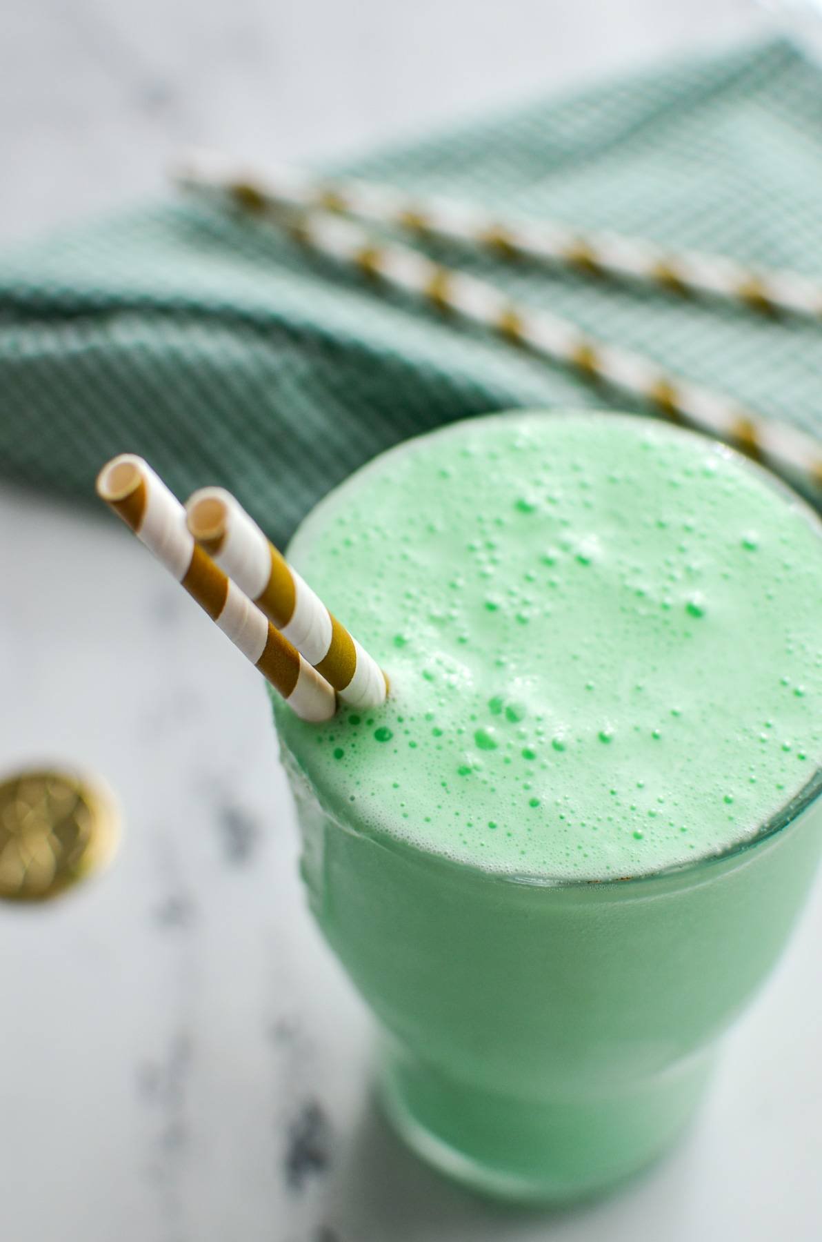 A large glass holding a green milkshake, with two straws sticking out of the side.