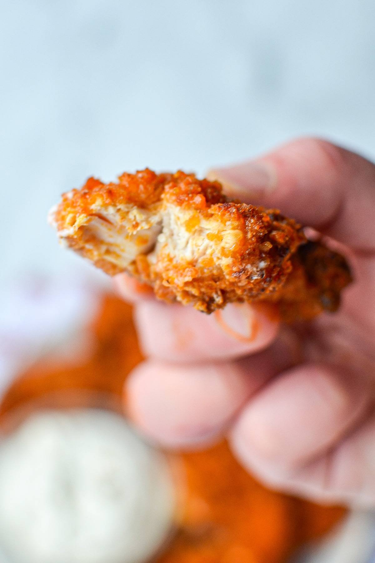 A piece of buffalo chicken tenders with a bite taken out of it.