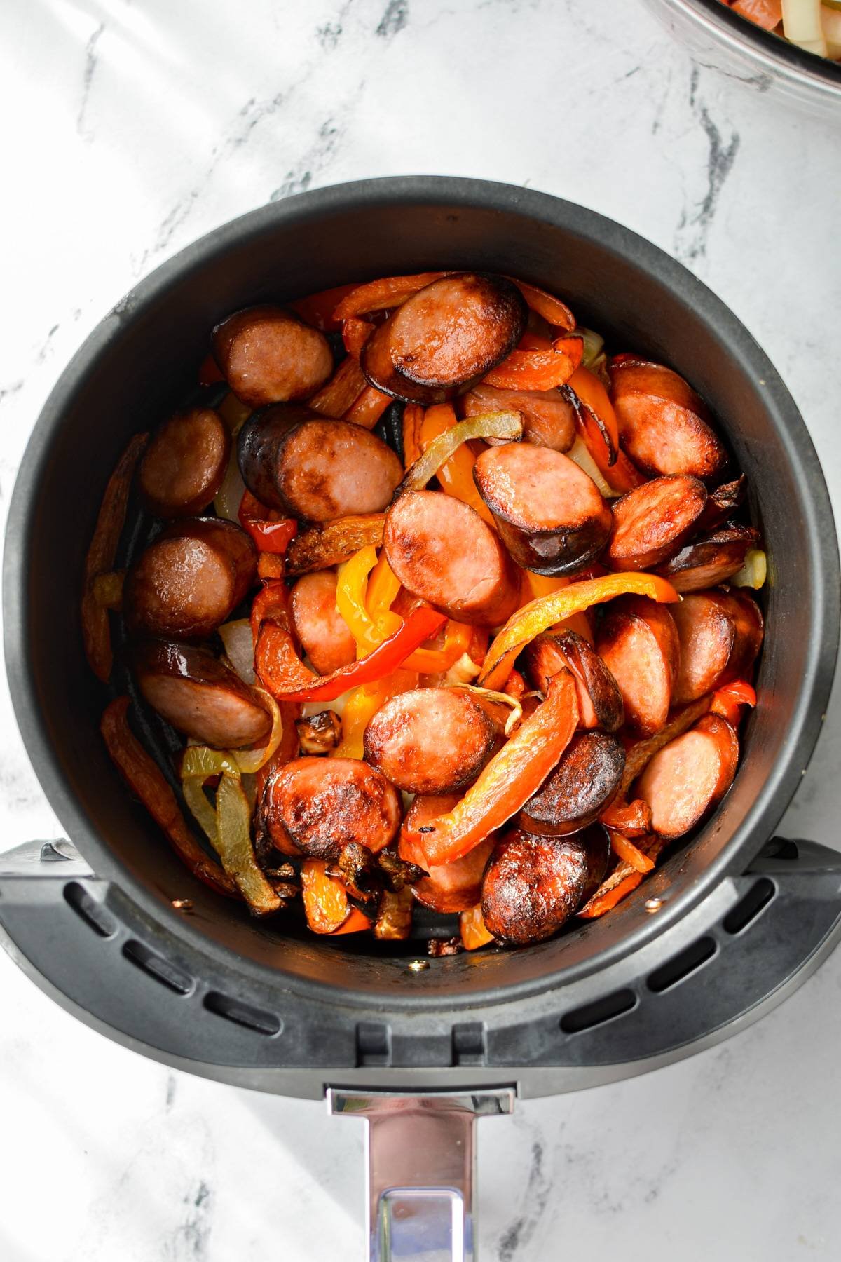 An overheat shot of an air fryer with cooked sausage and peppers.