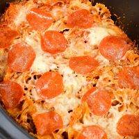 A close up of a slow cooker filled with pizza casserole, topped with pepperoni.