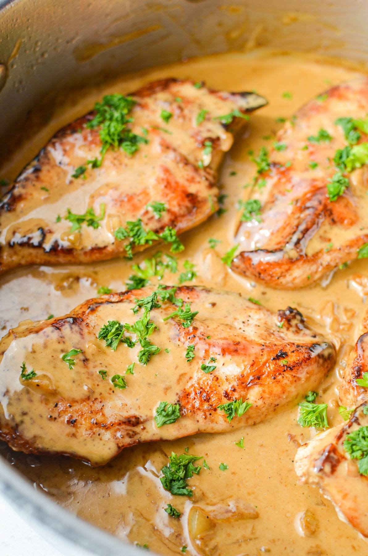 A close up of chicken in a skillet, coated in a light brown creamy garlic sauce.
