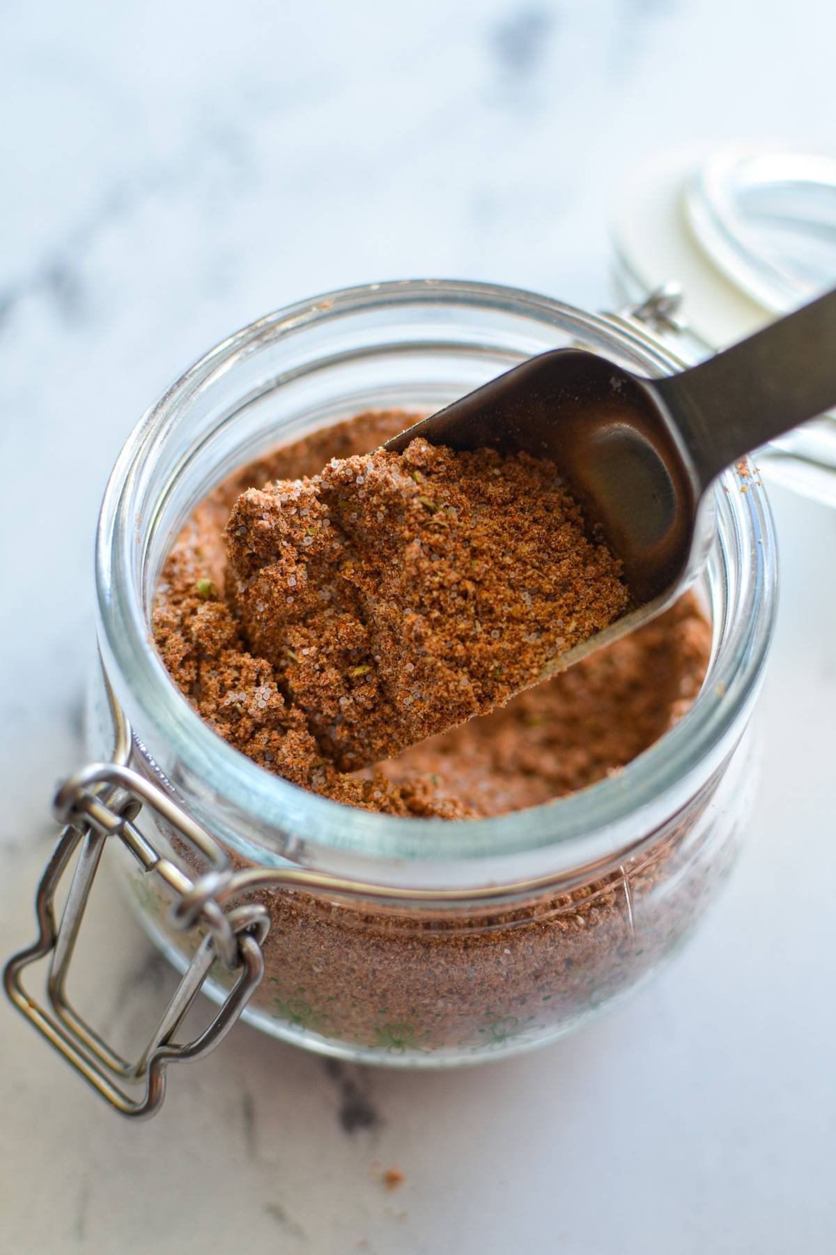 A small jar of taco seasoning with a spoon inside. 