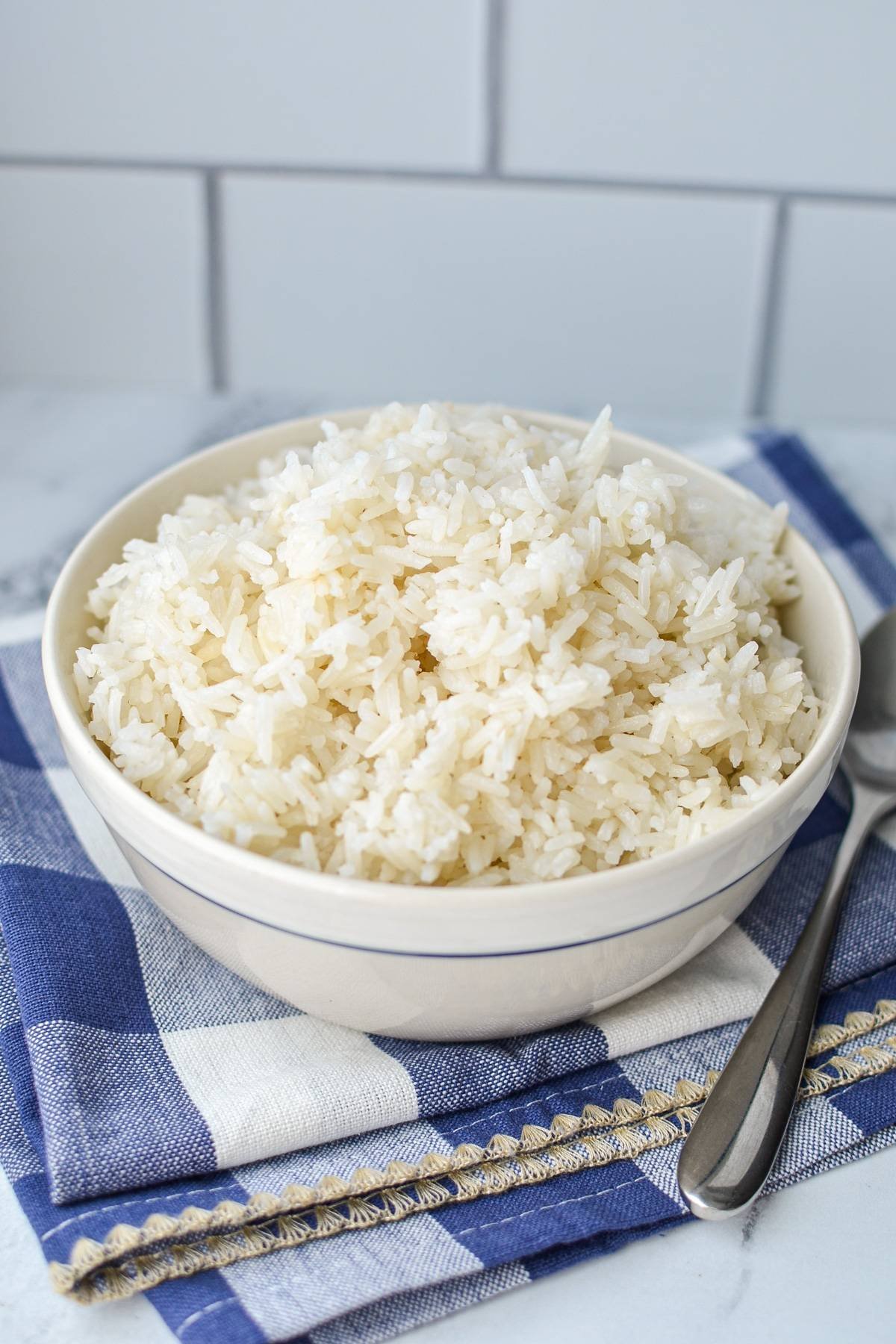 A bowl of white rice on a blue check napkin, with white tile in the background.