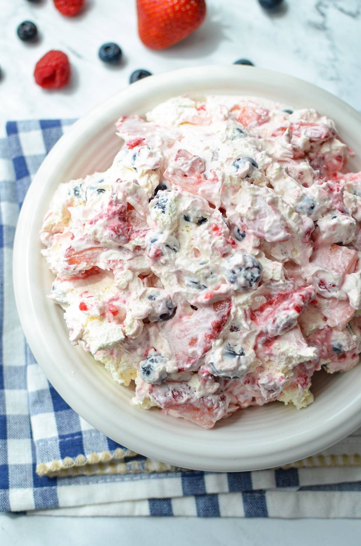 An overhead shot of a bowl of red white and blue cheesecake salad, with fresh berries on the counter next to it.