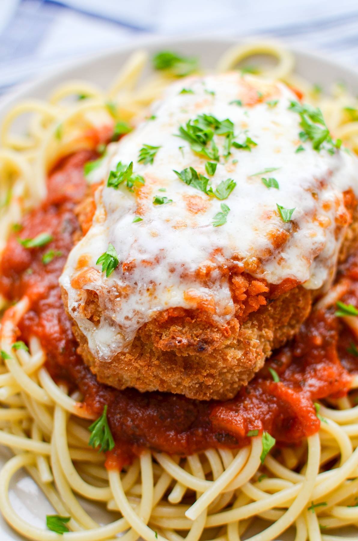 A cutlet of air fryer frozen chicken parmesan on top of a bed of cooked spaghetti.