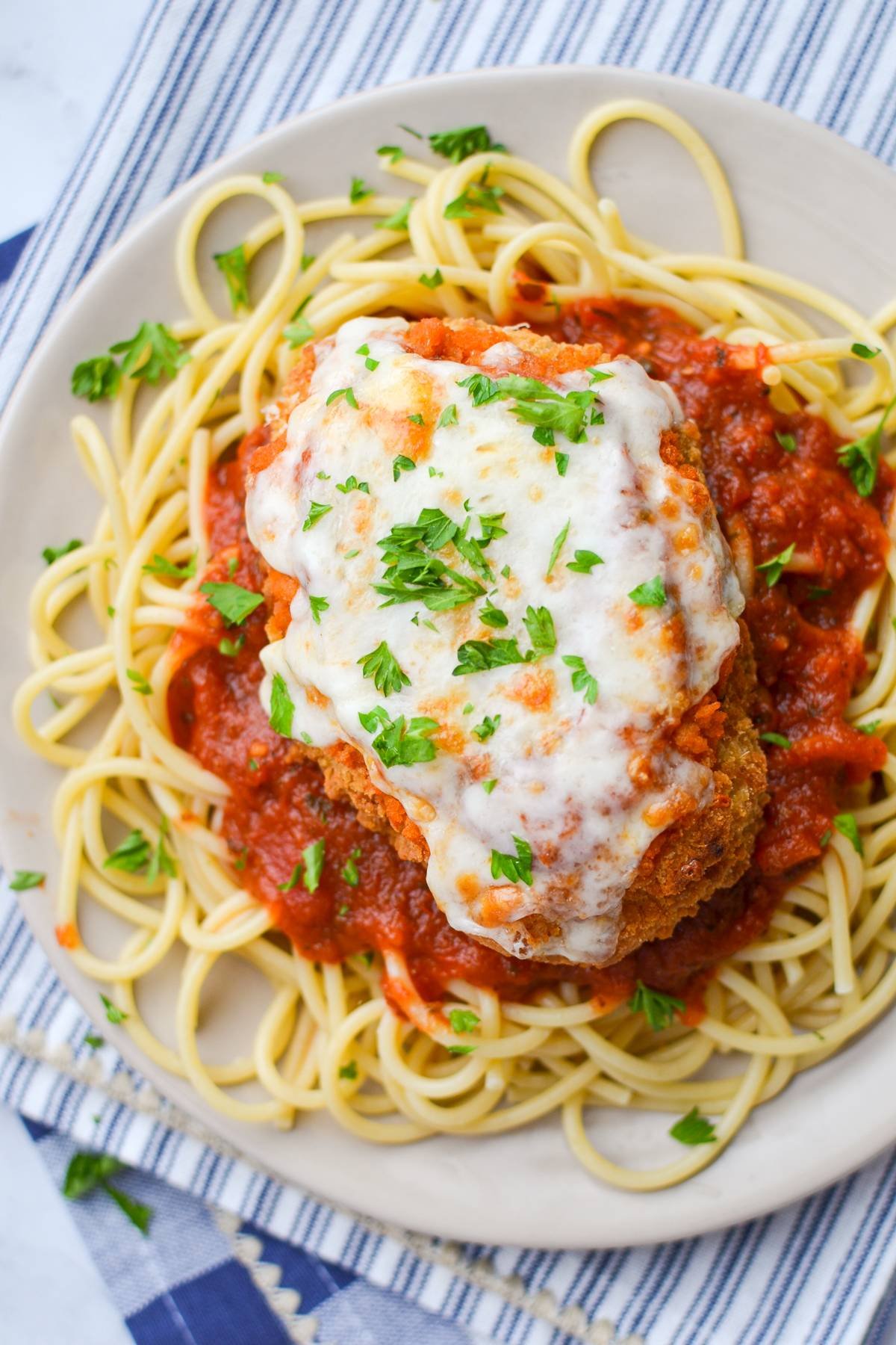 A plate of spaghetti noodles with chicken parmesan and marinara sauce.