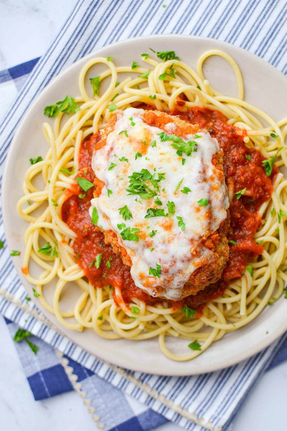 A plate of pasta with chicken parmesan, marinara and cooked pasta.