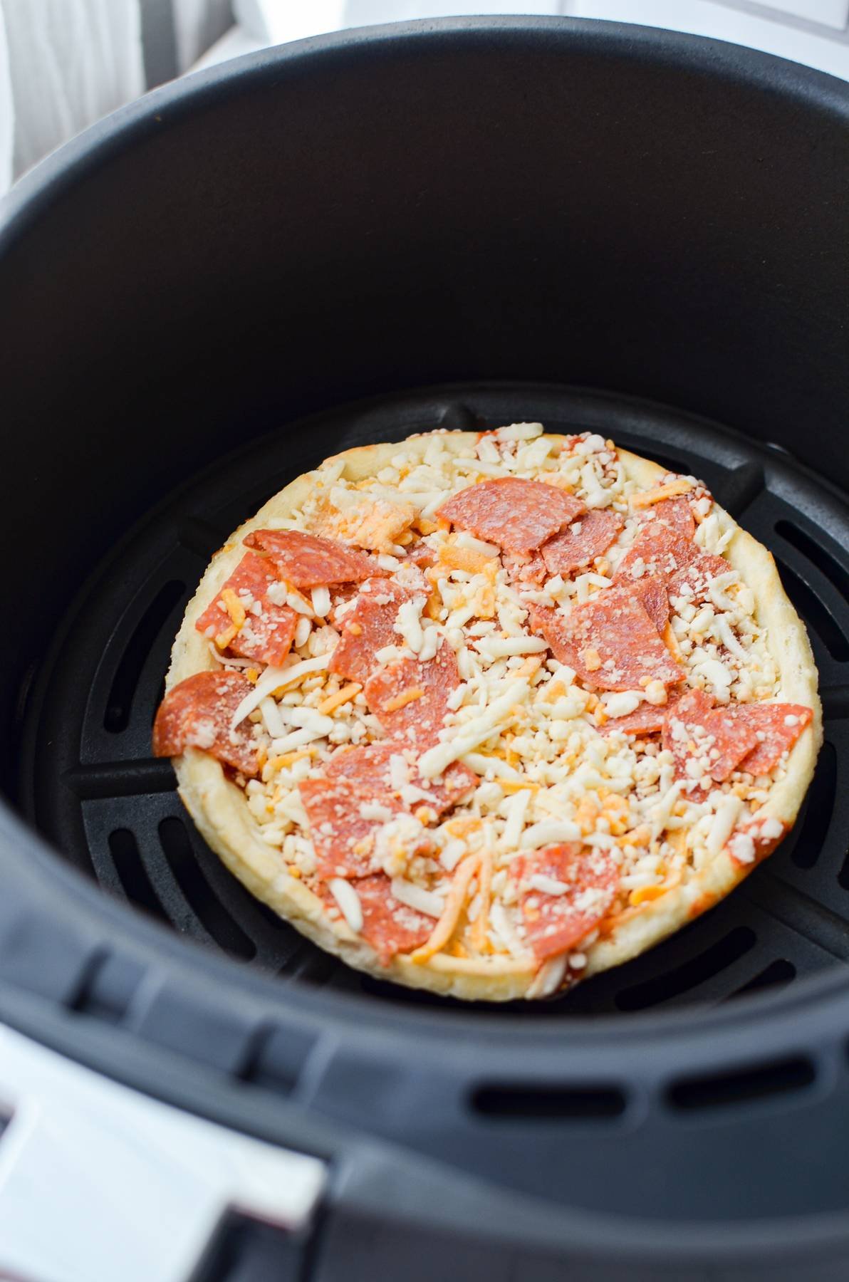 A frozen pizza in an air fryer basket.