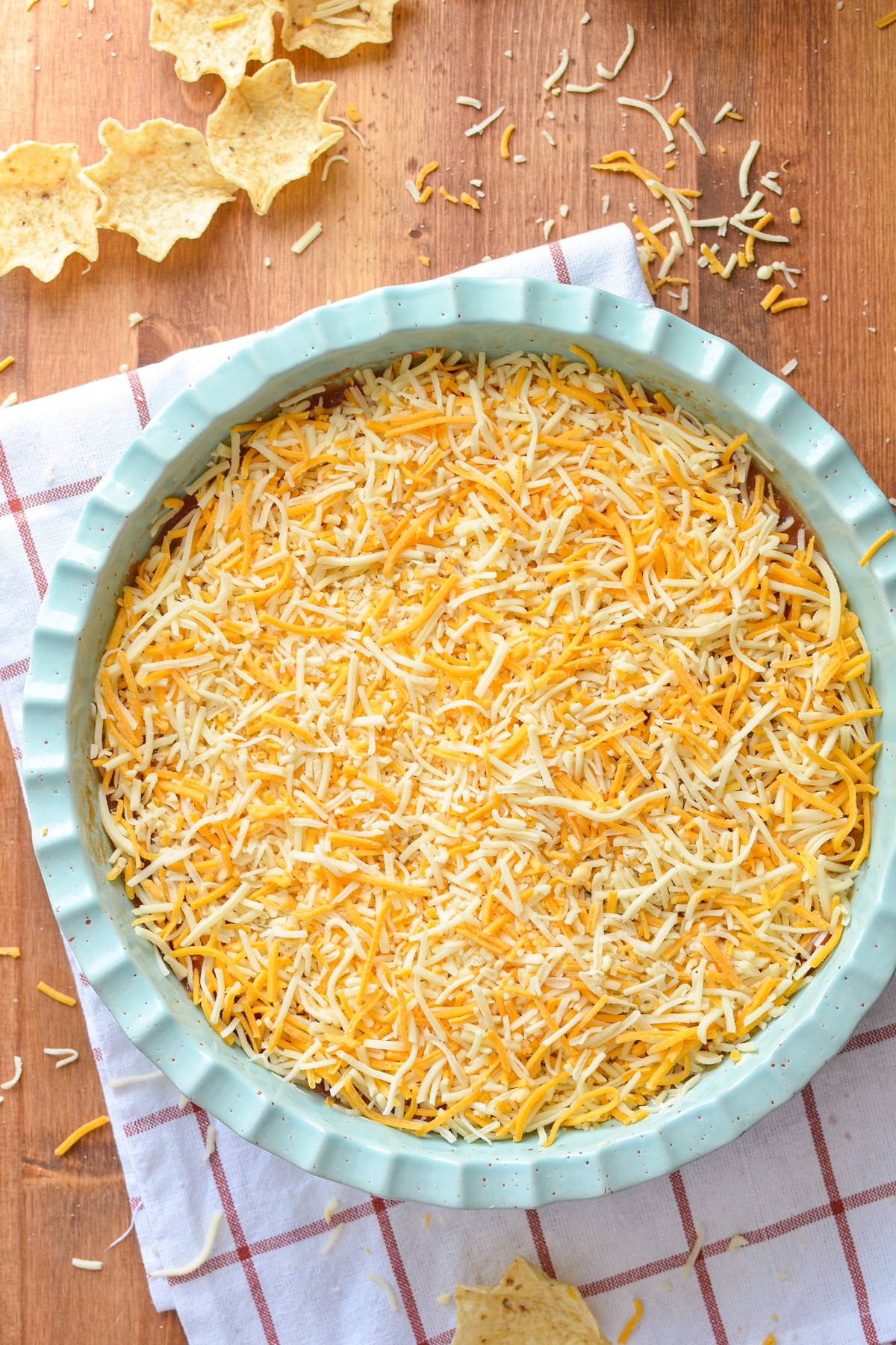 A circular dish filled with a nacho dip - topped with shredded cheese.