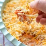 A chip being dipped into a cold salsa and cream cheese taco dip.