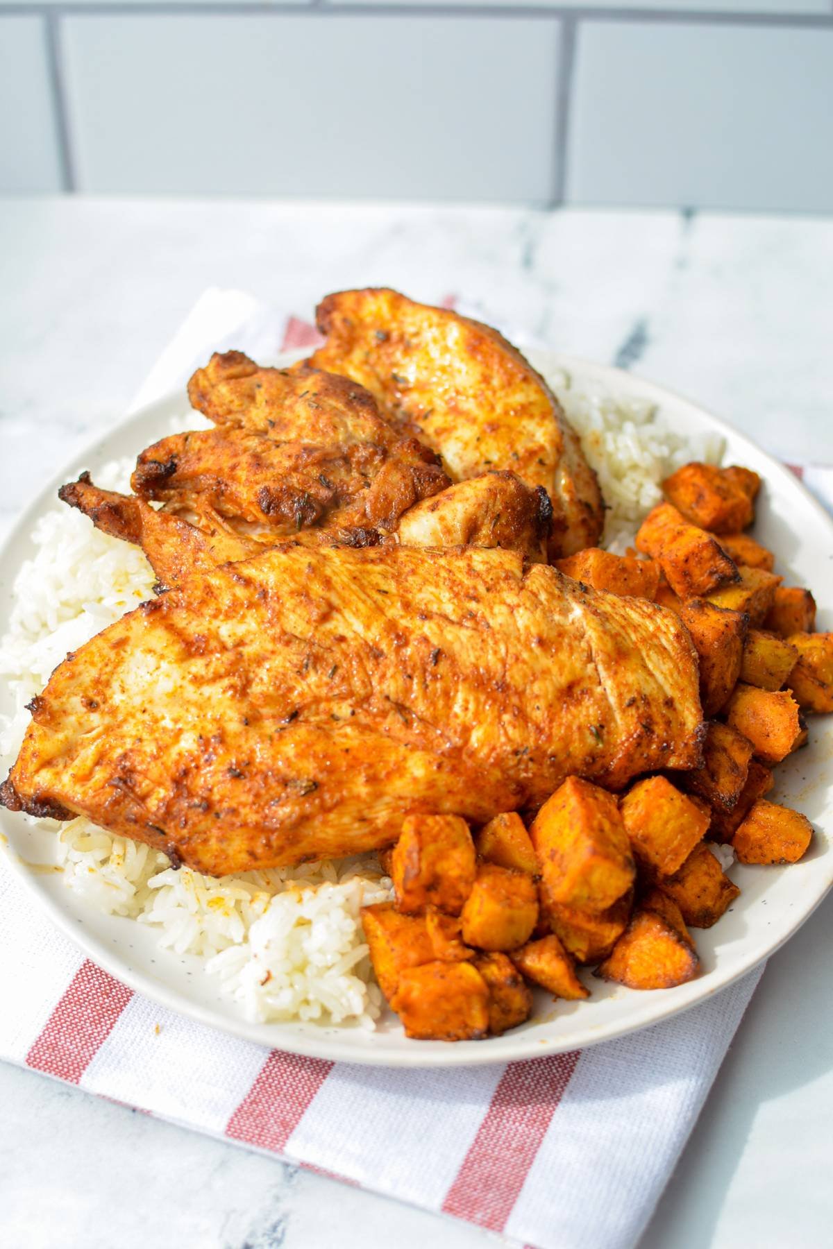 A plate filled with chicken, rice, and sweet potato cubes.