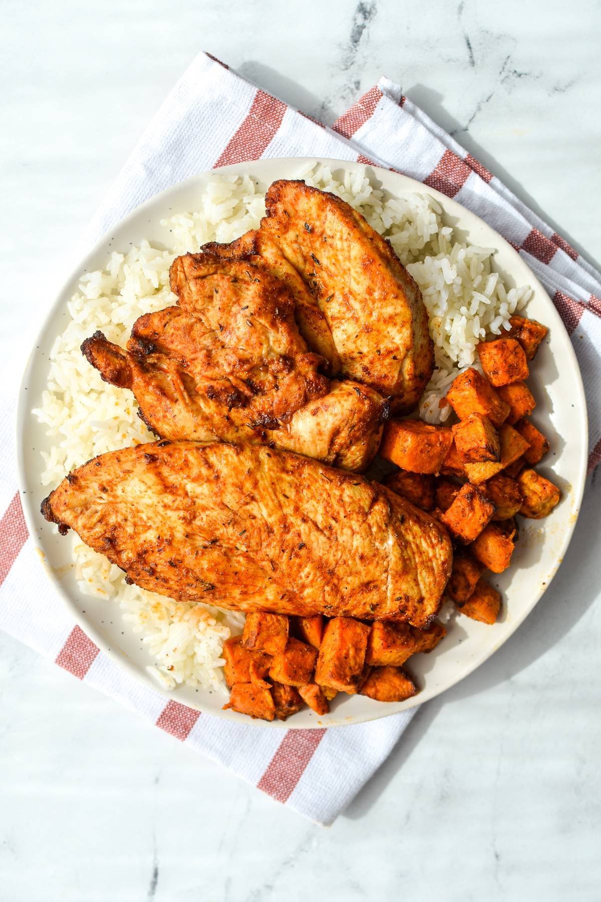 A plate filled with rice, sweet potatoes, and blackened chicken.