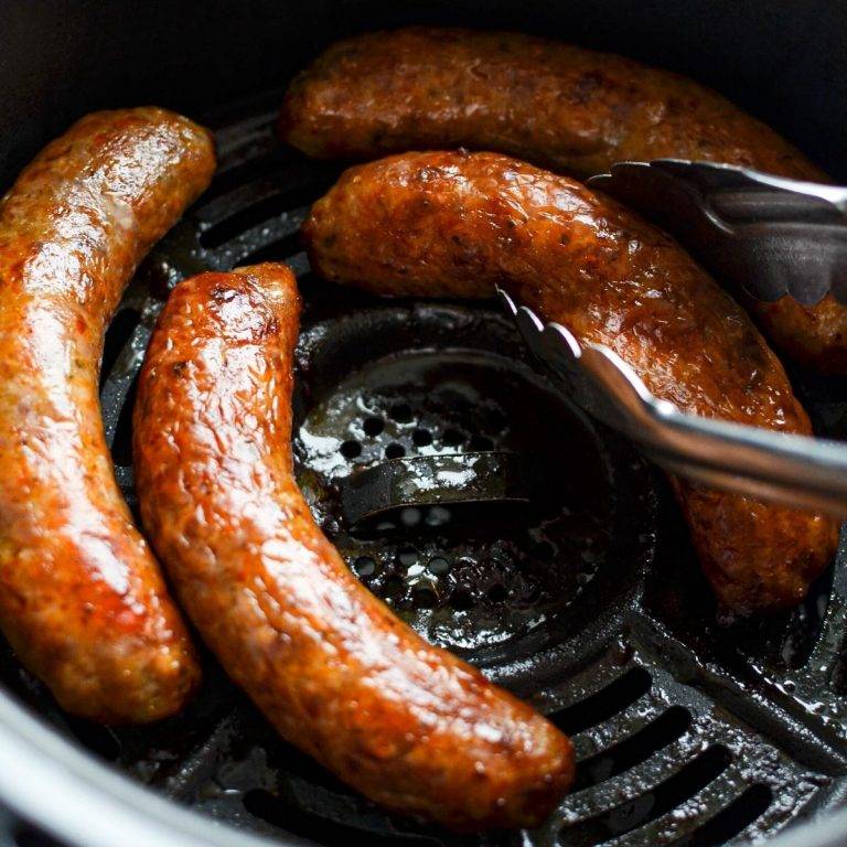 An air fryer basket with Italian sausages, being lifted out with tongs.
