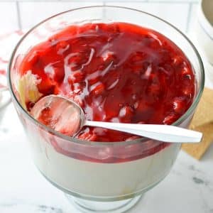 A trifle dish filled with no bake cheesecake and a cherry pie filling.