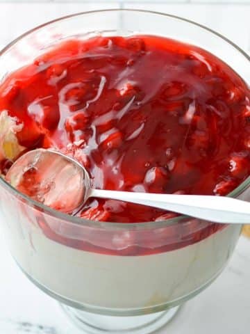 A trifle dish filled with no bake cheesecake and a cherry pie filling.