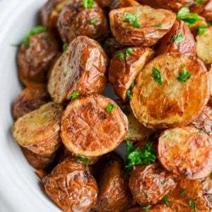 A bowl of halved and roasted baby potatoes garnished with parsley.
