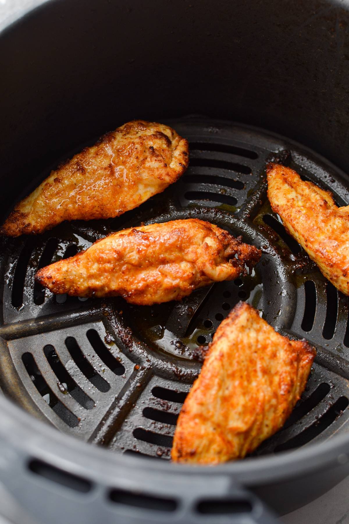 Fully cooked chicken tenders in an air fryer basket.