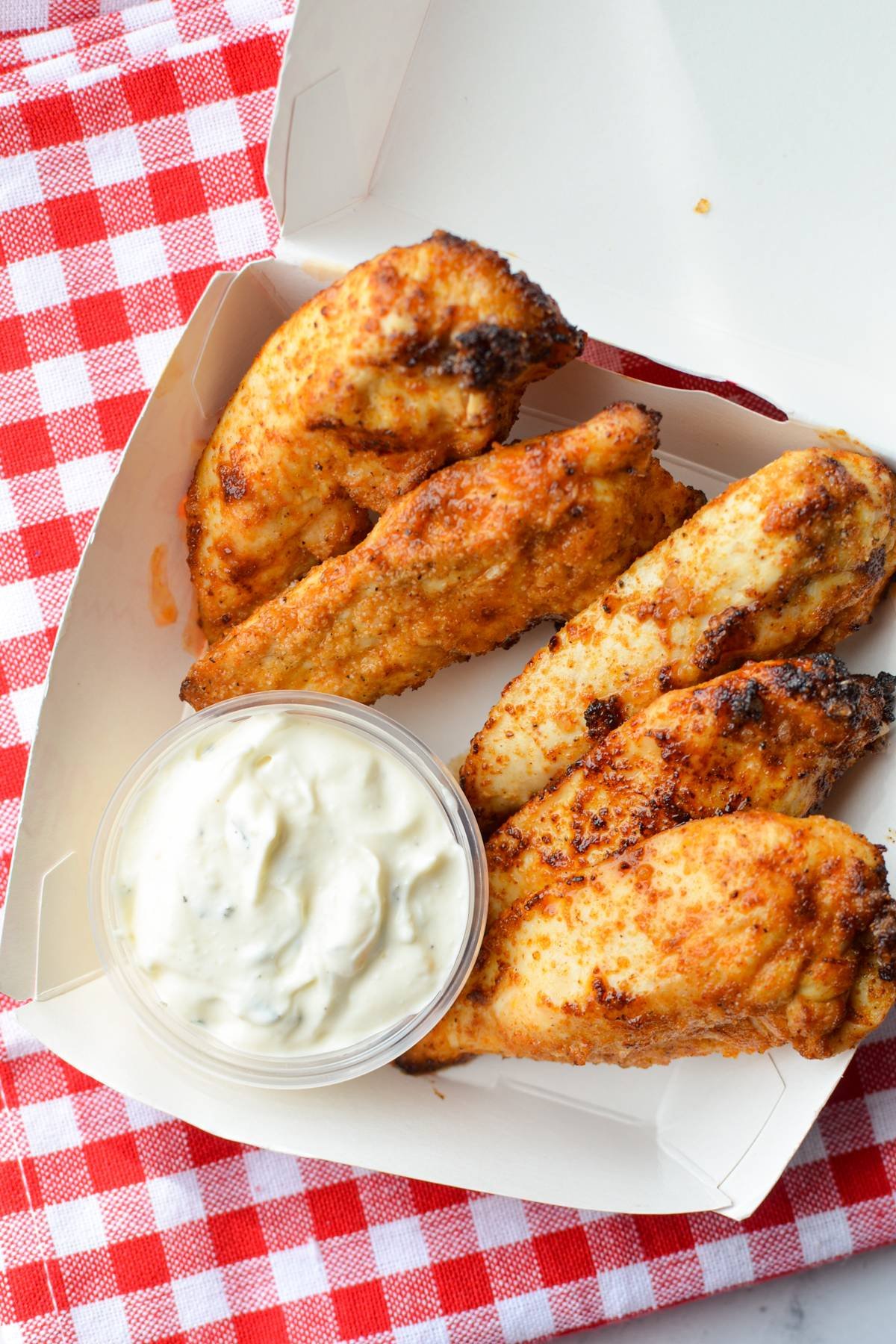 A small takeout box with homemade unbranded chicken tenders and ranch dip.