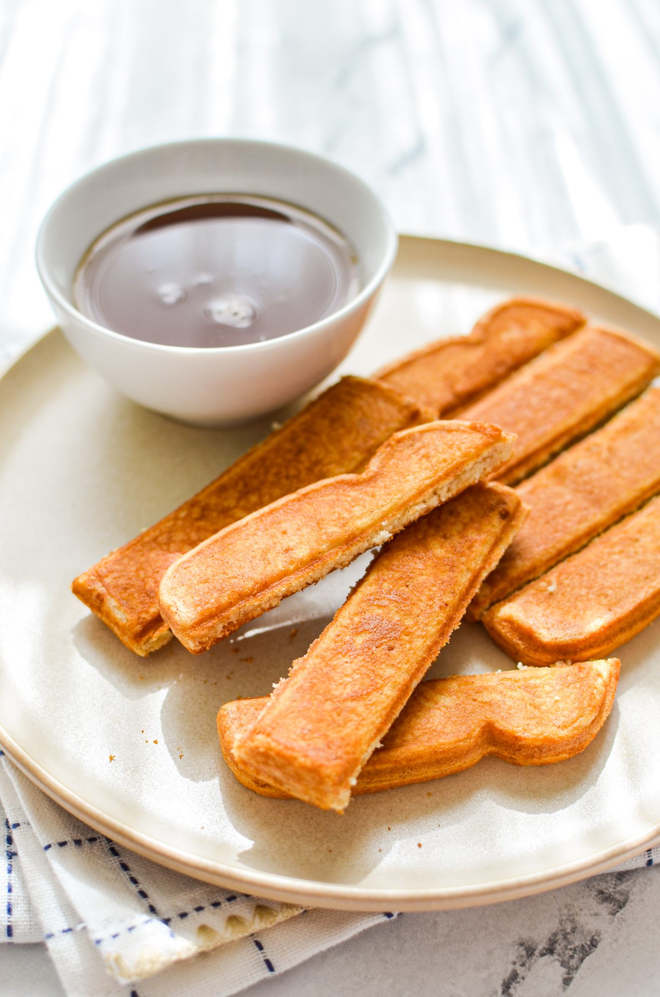 A plate of toast sticks with a bowl of maple syrup on the side.