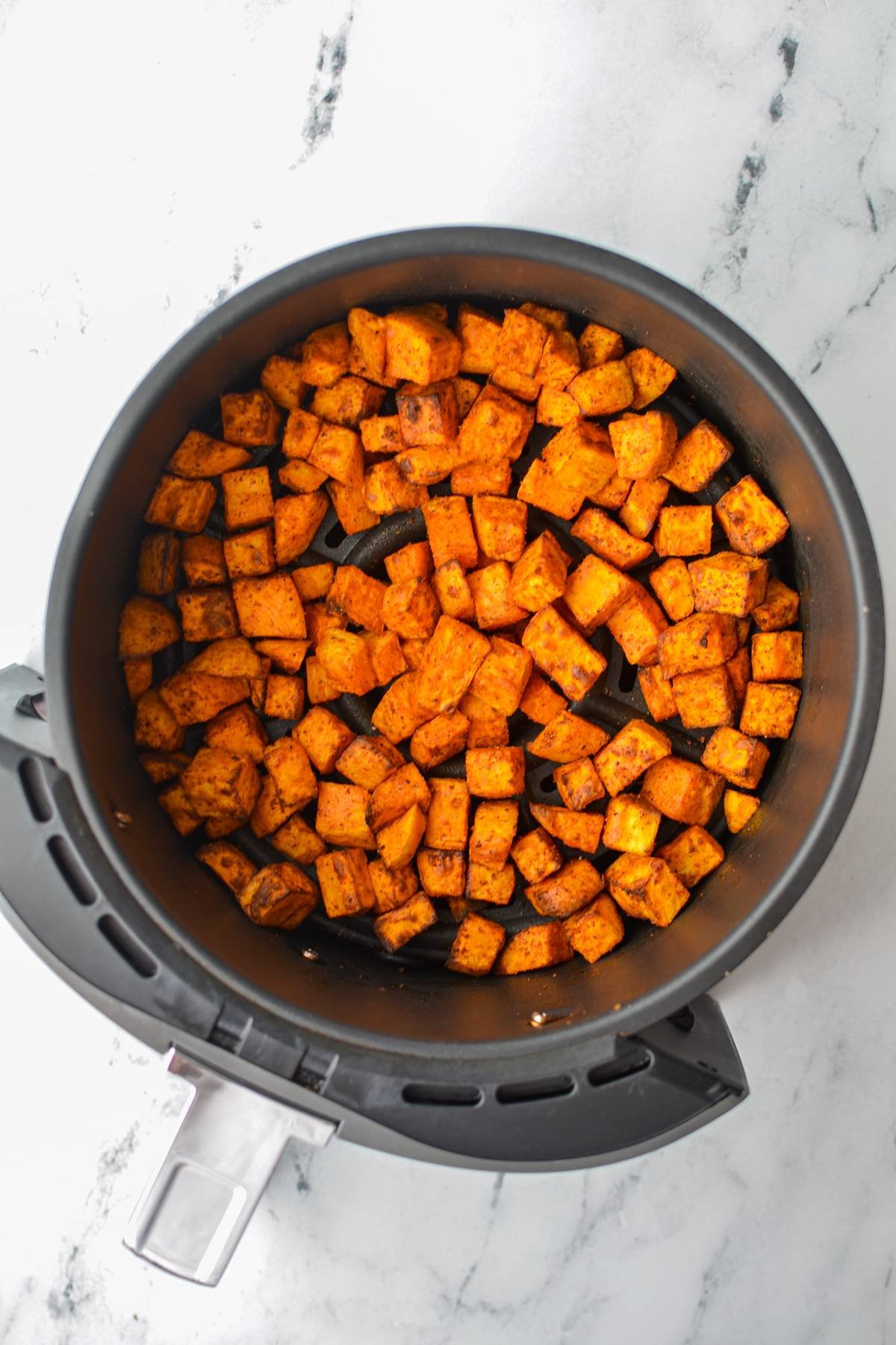 An air fryer basket with roasted sweet potato chunks.