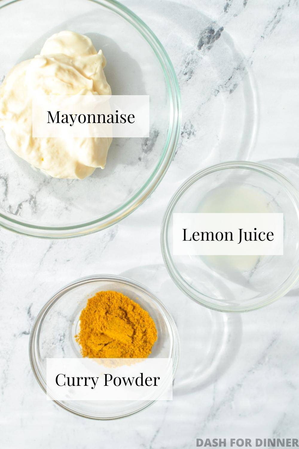 A small bowl of mayonnaise, another one of lemon juice, and a third with curry powder.