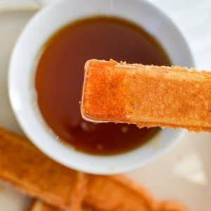 Dipping a French toast stick into a bowl of maple syrup.