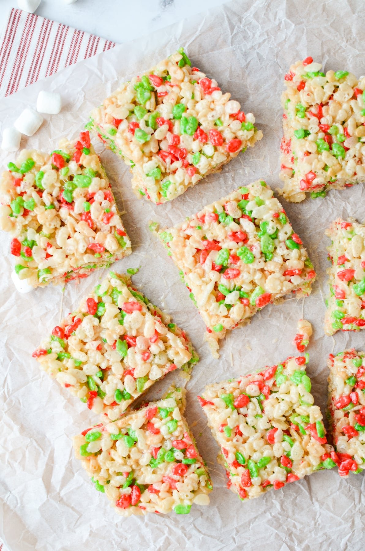 9 holiday Rice Krispies Treats cut on a piece of parchment.