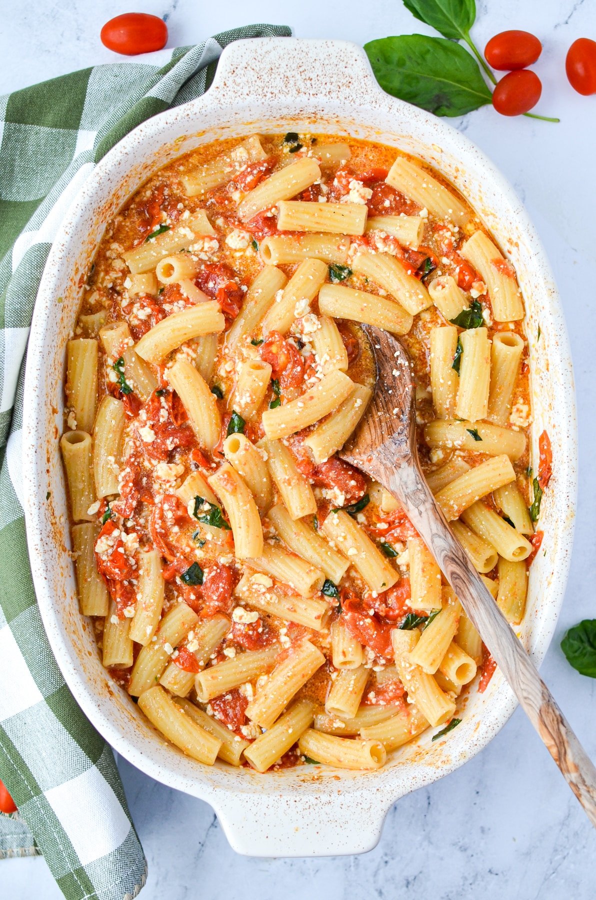 A baking dish with a tomato and pasta dish garnished with basil.