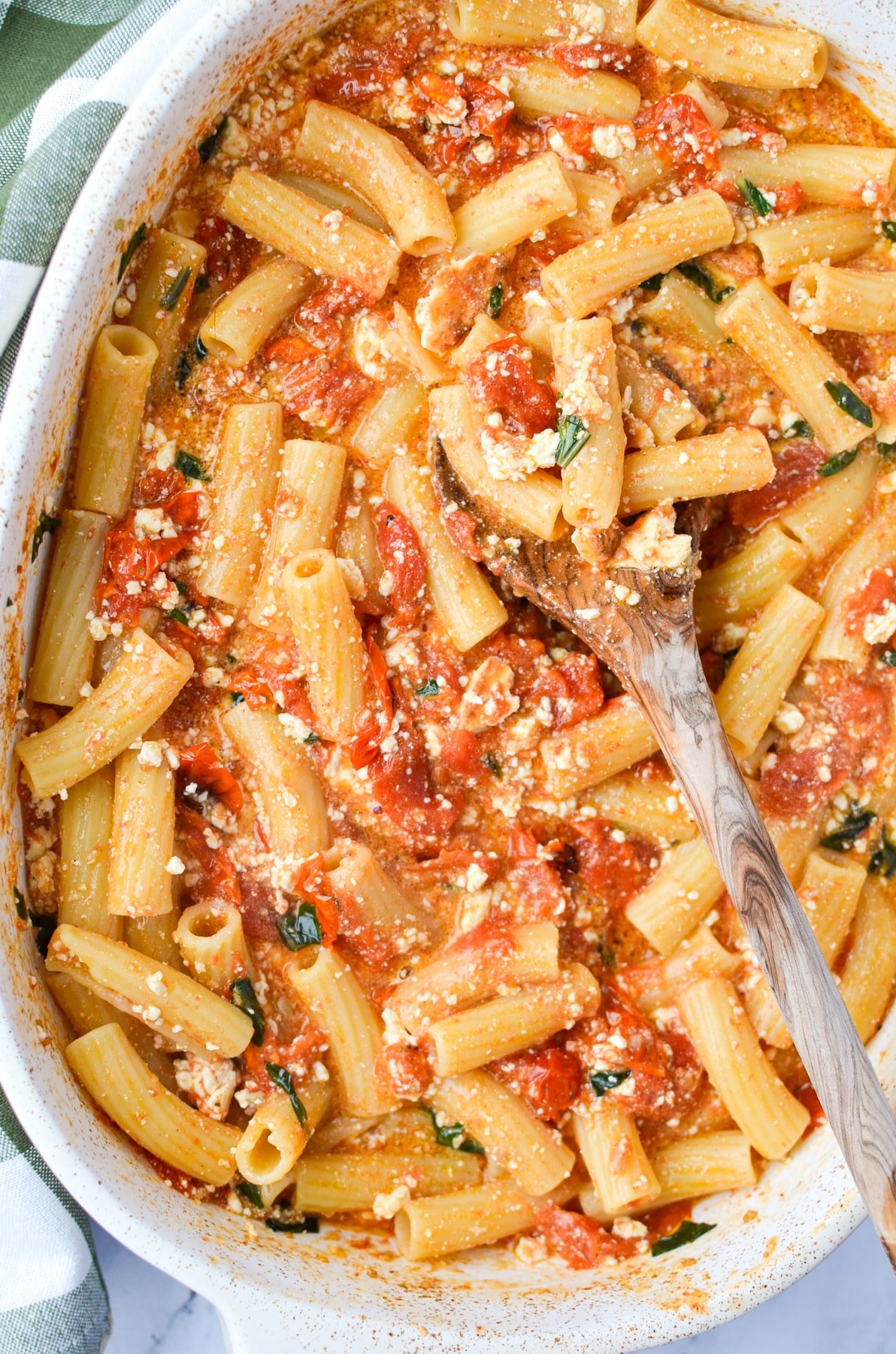 A baking dish with pasta, tomatoes, feta, and basil.