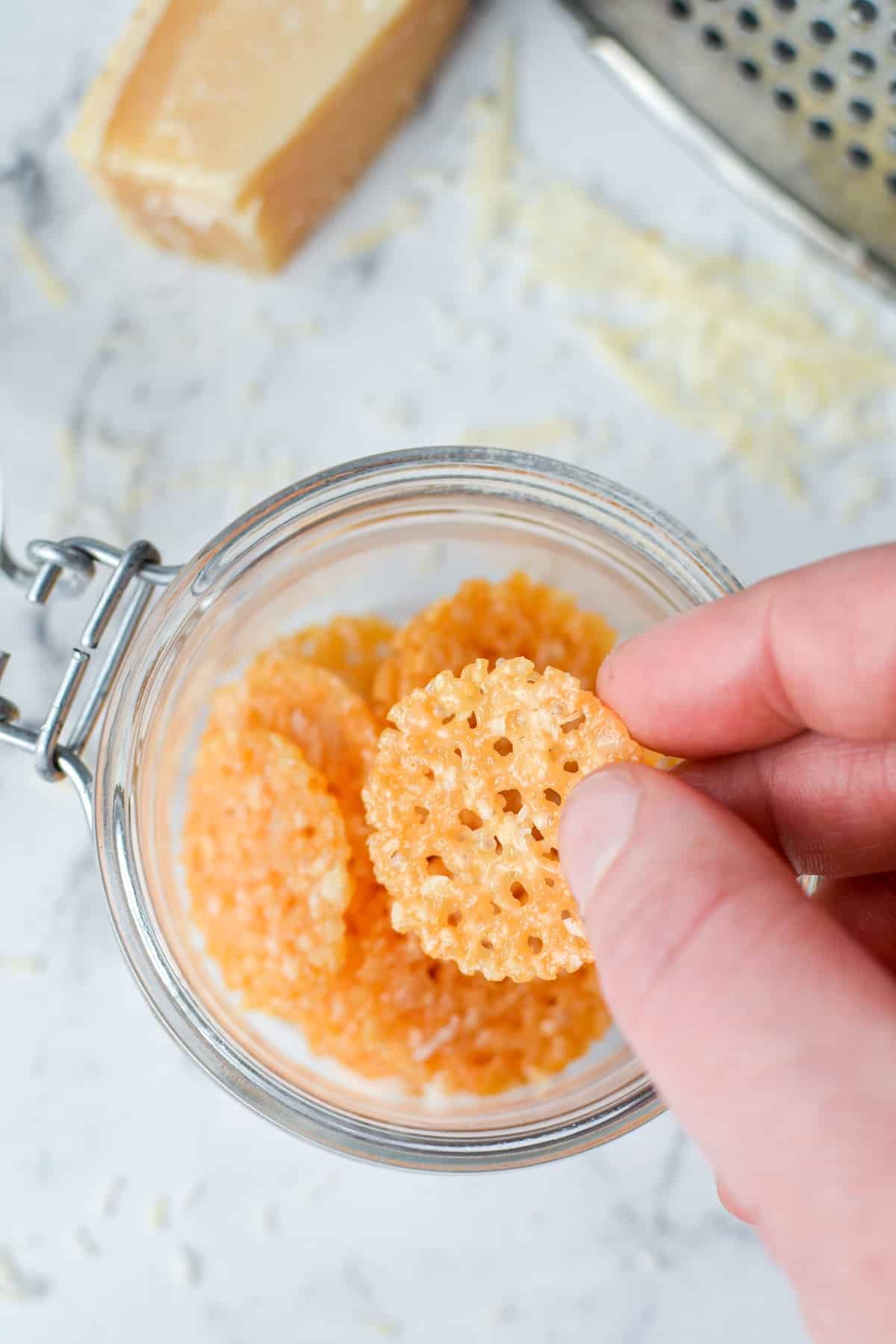 A hand taking a cheese chip from a jar.