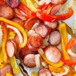 Tongs taking a portion of sausage rounds with peppers and onions.