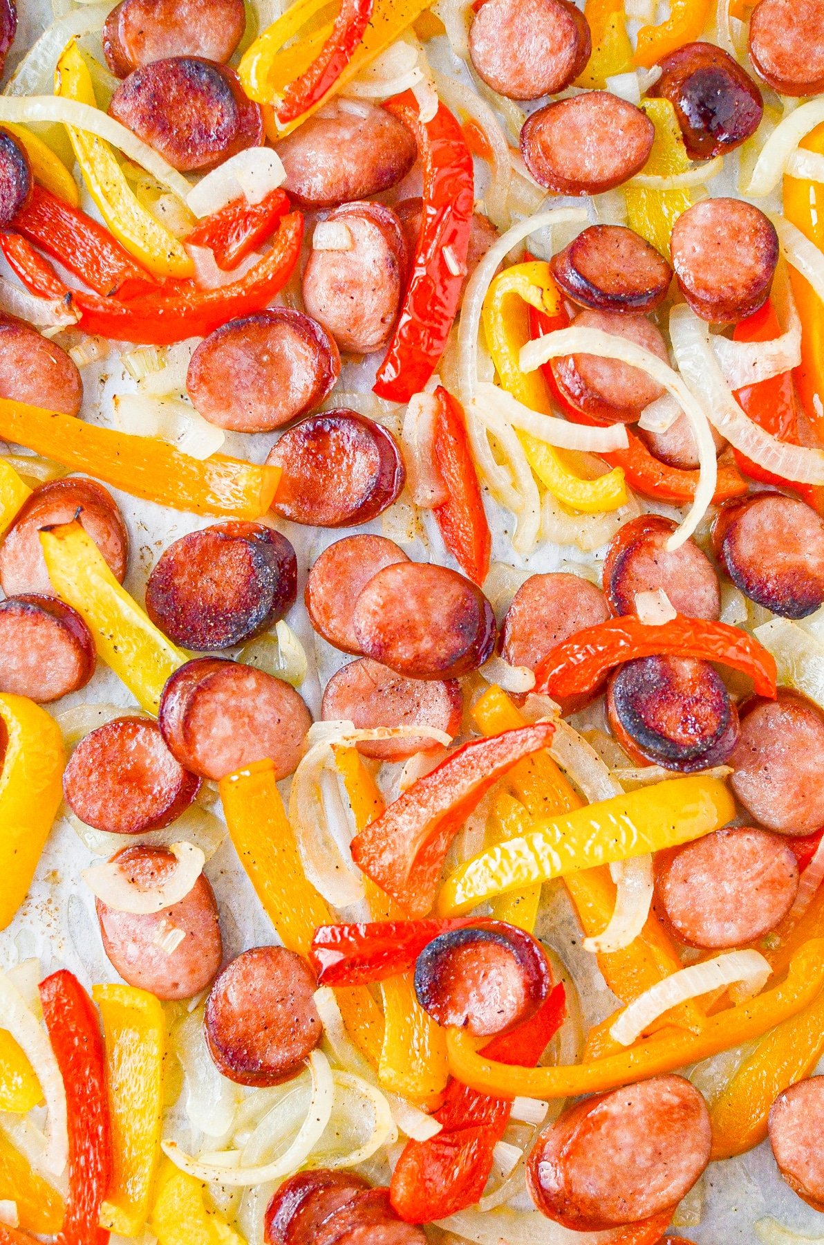 Sausage rounds, peppers, and onions on a sheet pan.