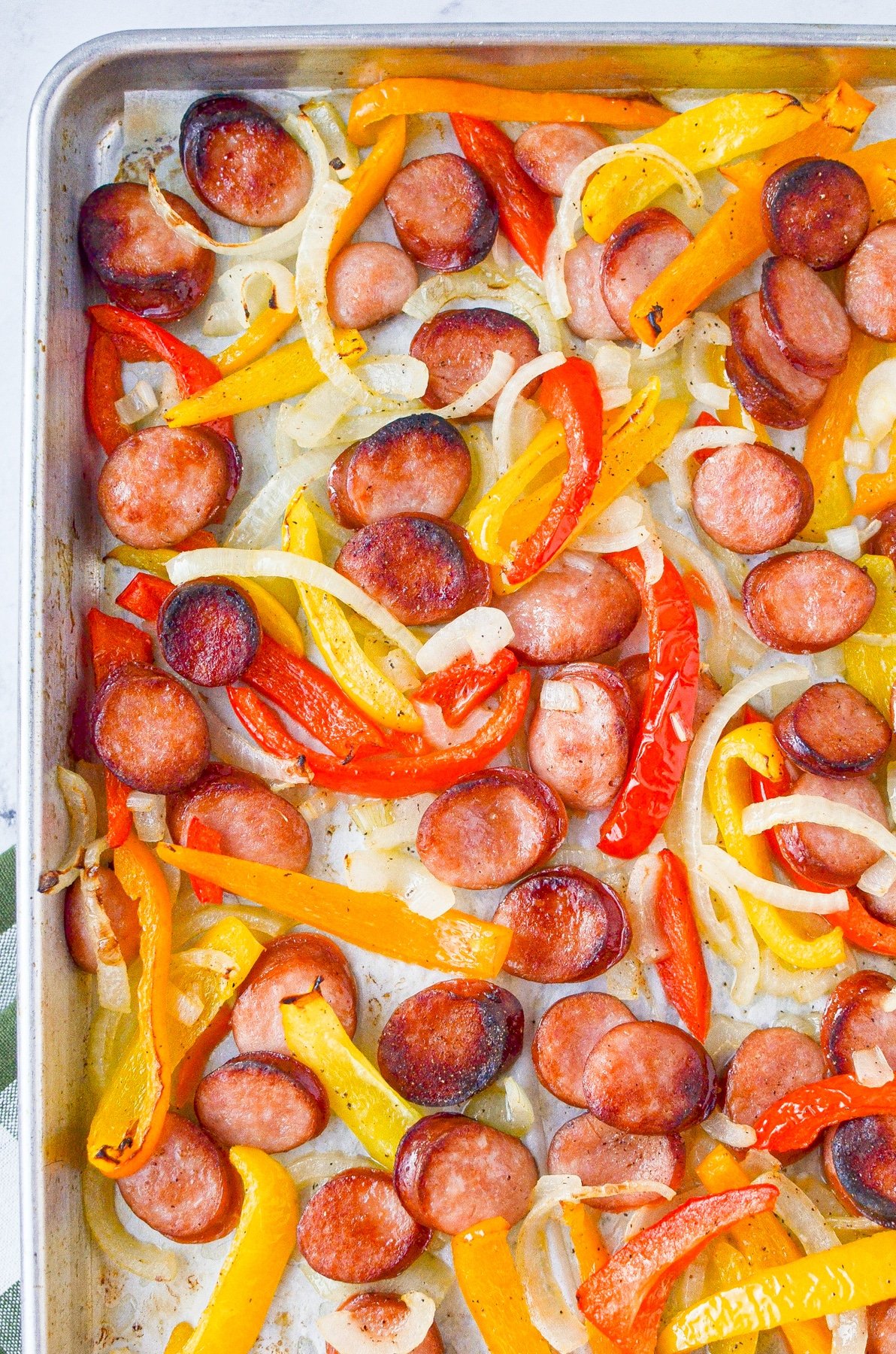 A sheet pan filled with sliced sausages, bell peppers, and onions.
