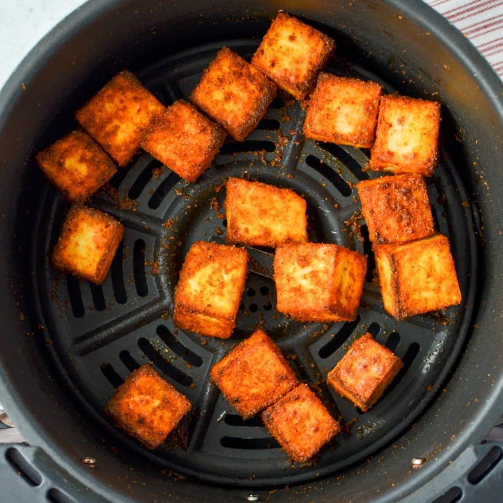 An air fryer basket with paneer cubes in it.