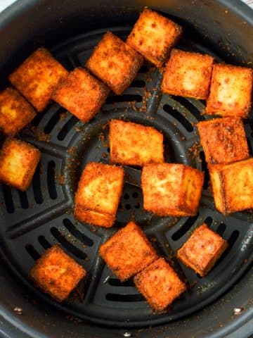 An air fryer basket with paneer cubes in it.