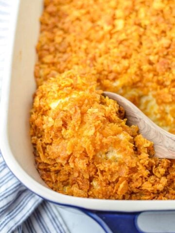 Scooping out hash brown casserole with a wooden spoon.