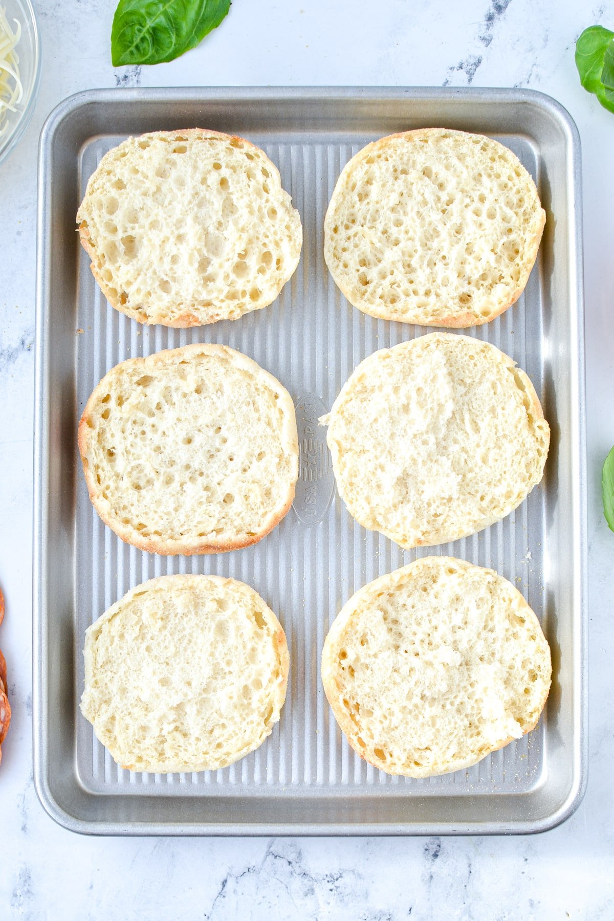 A baking sheet with English muffin halves on it.