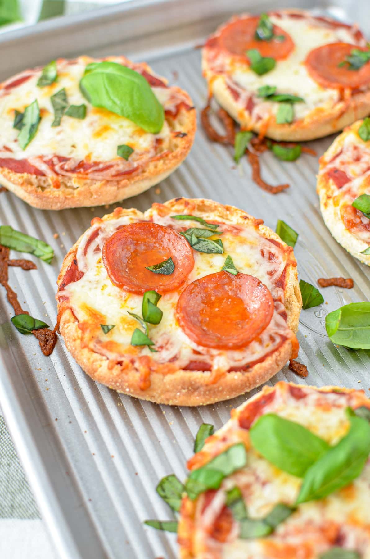 A close up of a mini pizza topped with pepperoni and basil.