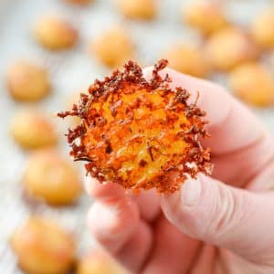 A hand holding a halved baby potato encrusted with parmesan cheese.