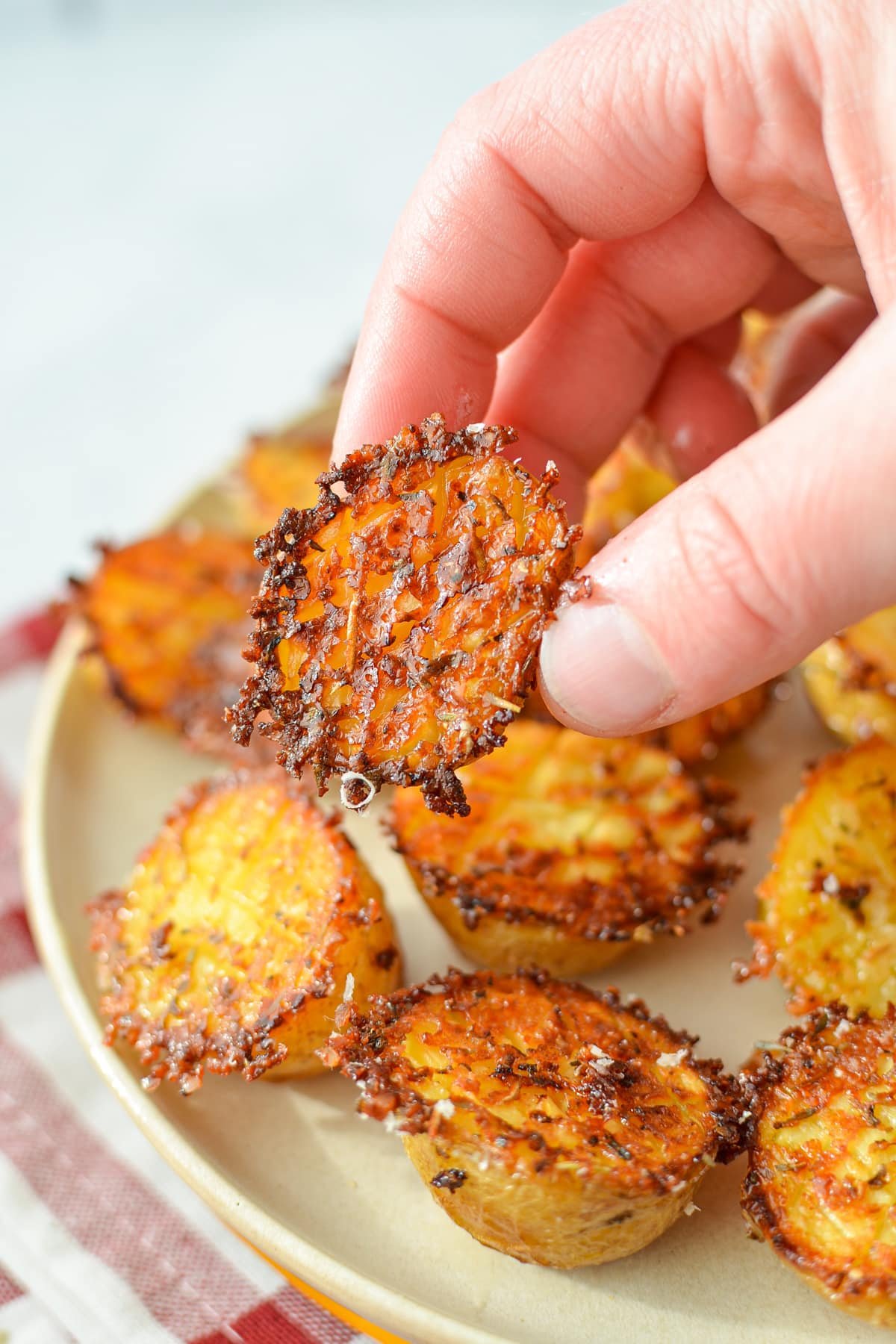 A hand taking a small potato from a plate of roasted parmesan potatoes.