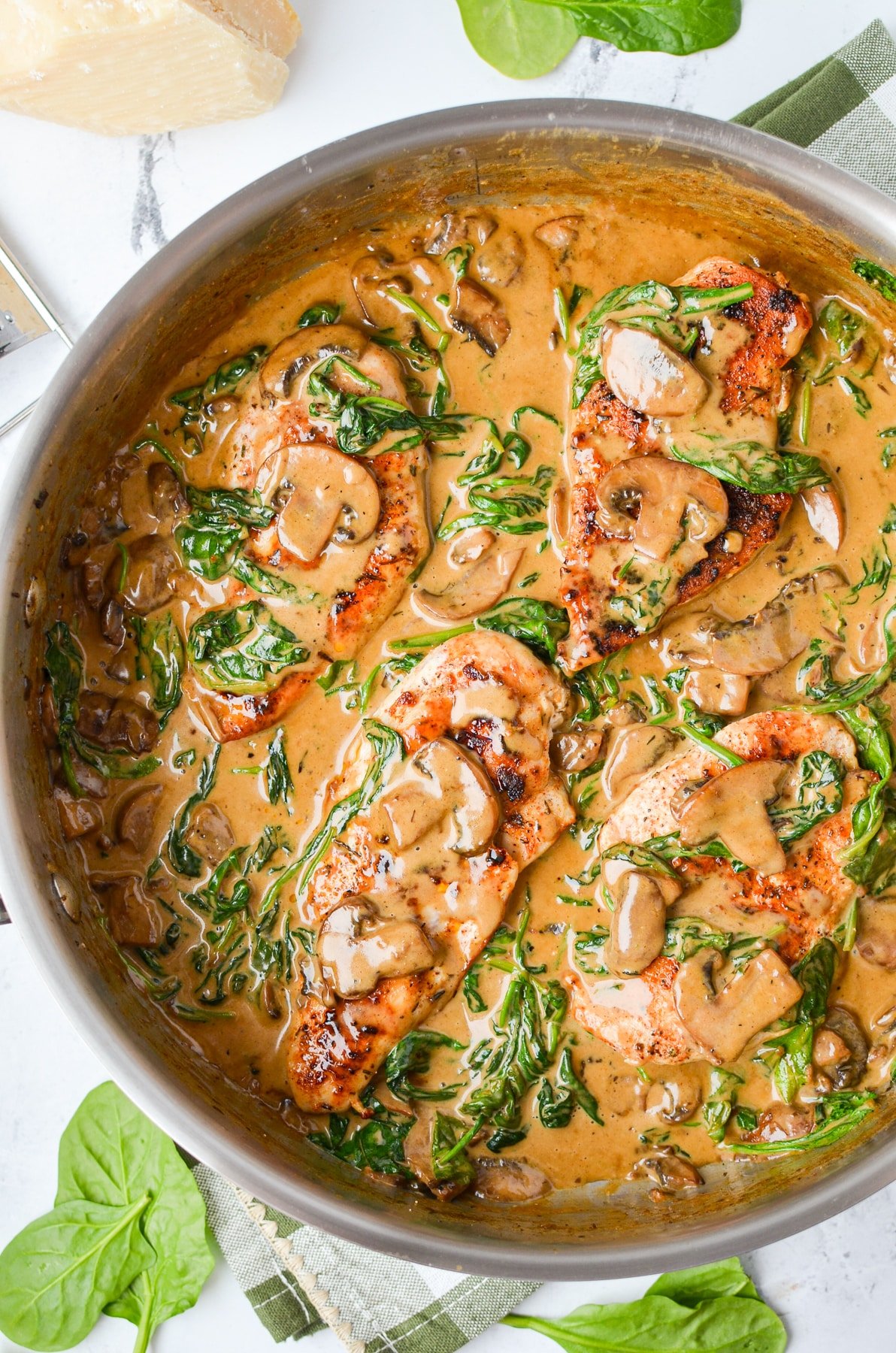 A skillet with chicken covered in a spinach and mushroom cream sauce.