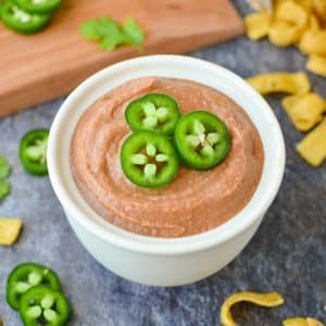 A bowl of bean dip garnished with sliced jalapeños.